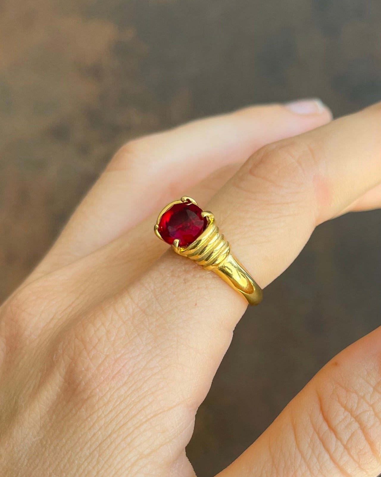 Gold ring with a red gemstone on a neutral background