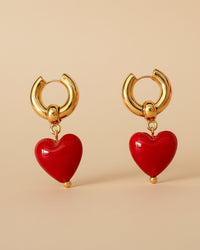 Thumbnail for Gold hoop earrings with red heart charms on a beige background