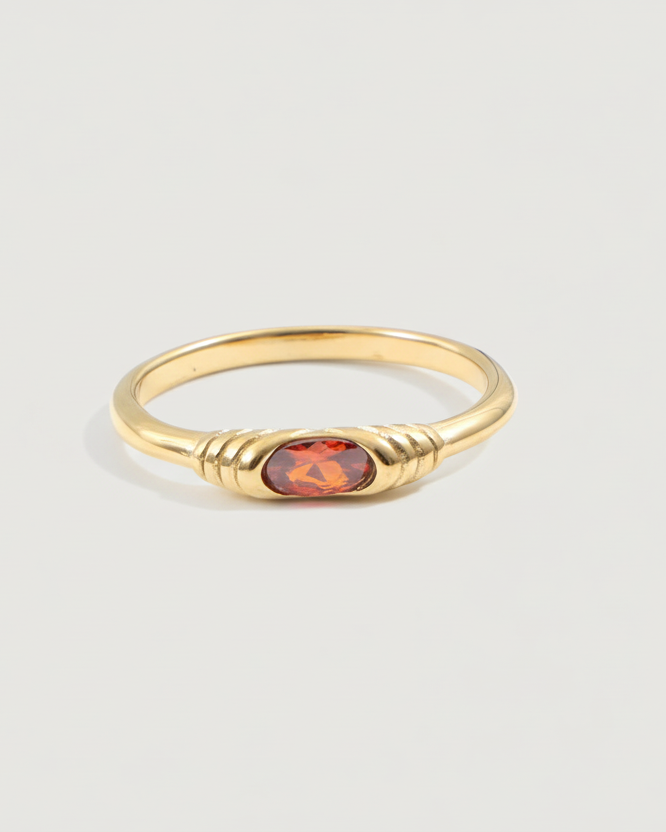 Gold ring with a red gemstone on a light gray background