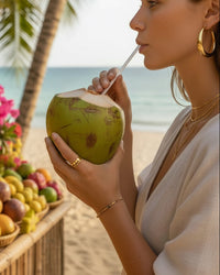 Thumbnail for Woman drinking from a coconut on a beach with palm trees and fruit in the background