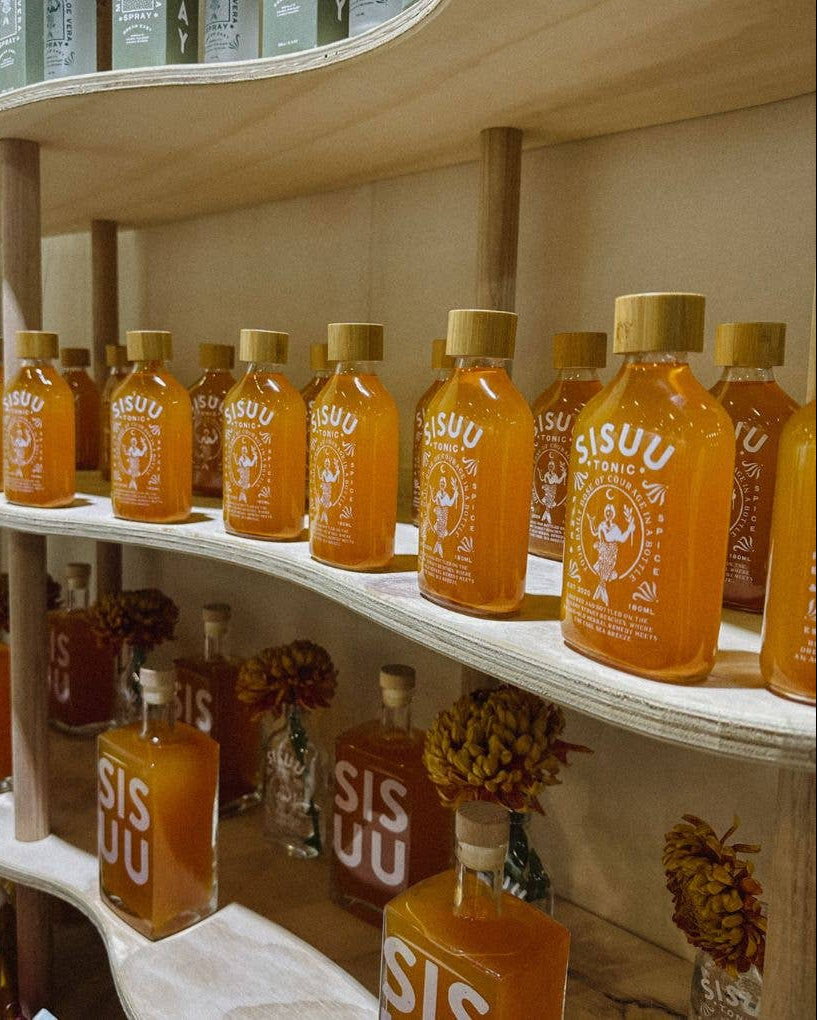 Shelf displaying multiple bottles of SISUU on a wooden shelf with a neutral background.