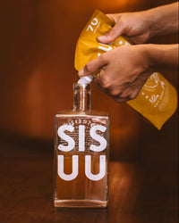 Thumbnail for Person pouring a liquid from a yellow bag into a clear bottle labeled 'SIS U' on a wooden surface.