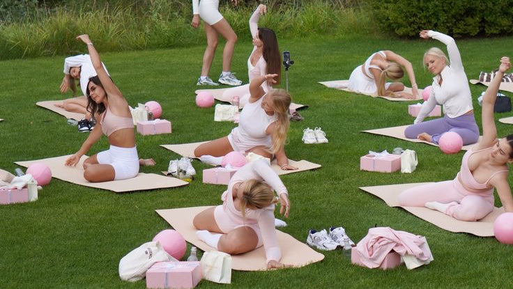 Group of people practicing yoga outdoors on a grassy area with trees in the background