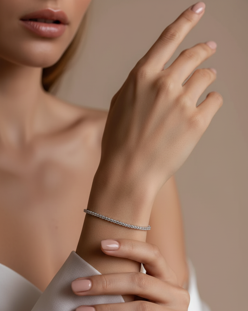 Close-up of a hand wearing a silver tennis bracelet on a neutral background