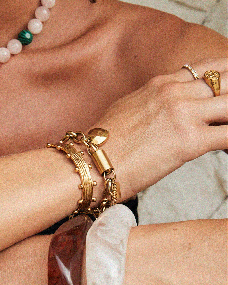 Close-up of a person wearing gold bracelets, a pearl necklace, and a large wooden bracelet.
