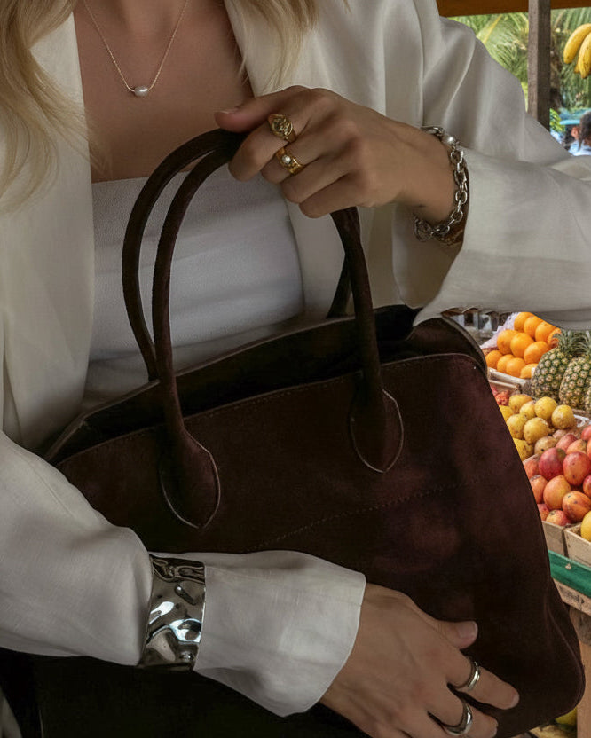 Close-up of a person holding a brown handbag with visible jewelry.