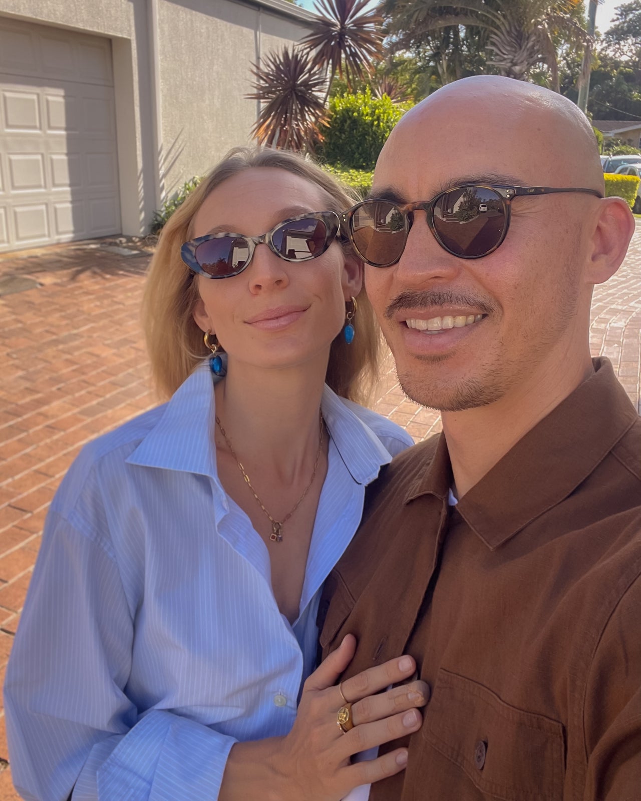 Jodie wearing OCEAN_WAVE_HEART_DROP_EARRINGS_BLUE 
sunglasses outdoors with a house and plants in the background