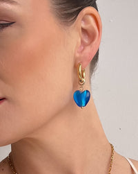 Thumbnail for nikki wearing a gold necklace and blue heart-shaped earrings against a plain background