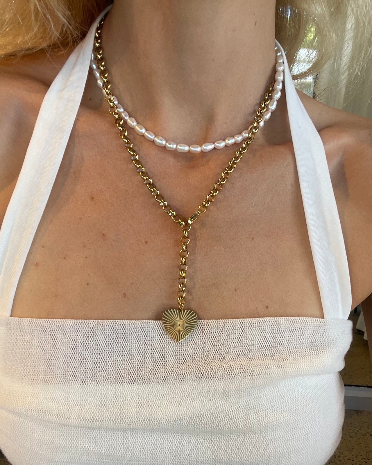 Woman wearing a gold necklace with a heart pendant on a white dress.
