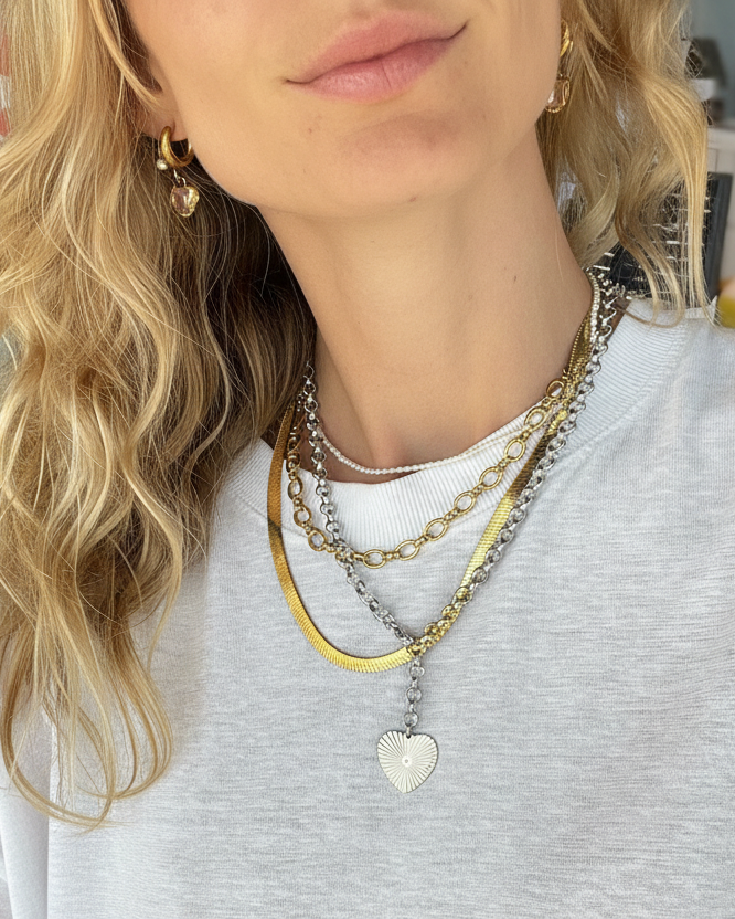 Person wearing multiple necklaces with a heart pendant, against a neutral background.