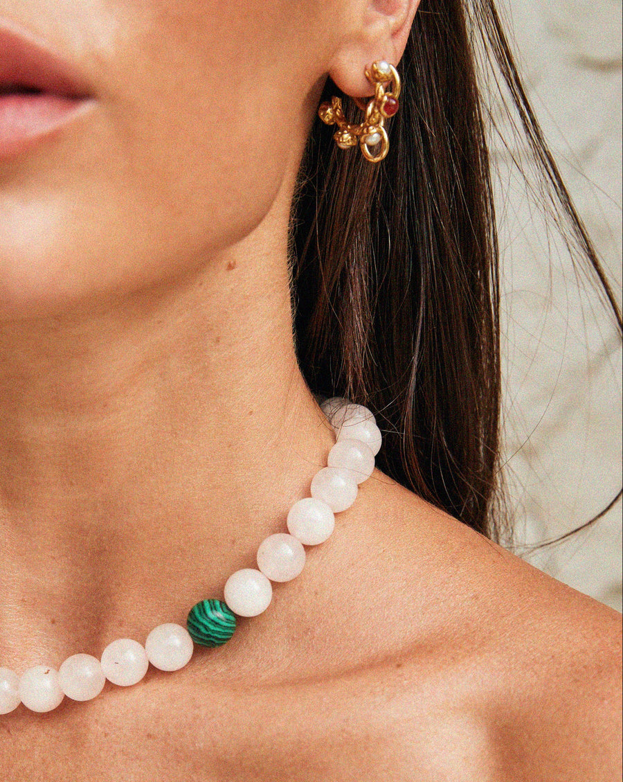 Close-up of a Tilly Smith wearing a pearl necklace with a green stone and gold earrings.