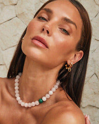 Thumbnail for Tilly Smith wearing a pearl necklace and gold earrings against a stone wall.