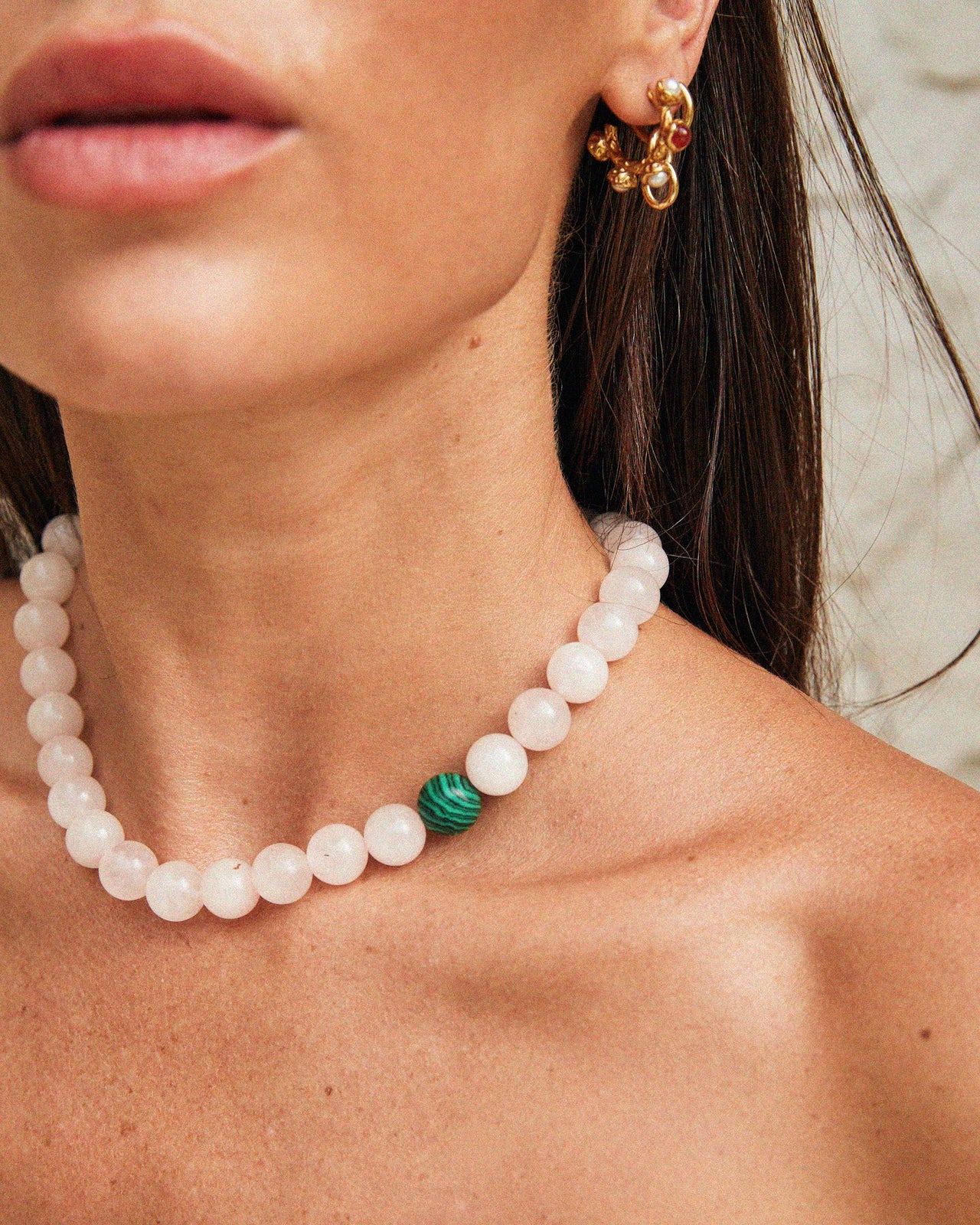 Close-up of a Tilly Smith wearing a pearl necklace with a green stone and gold earrings.