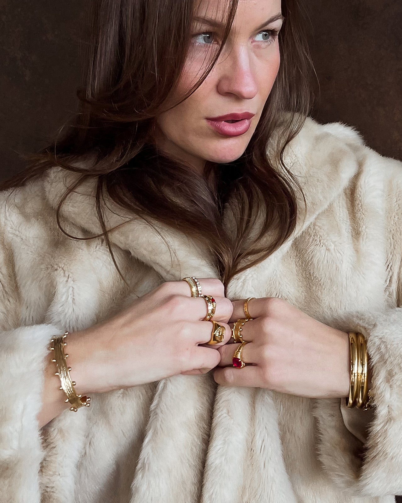 nikki wearing multiple gold rings and bracelets on a neutral background