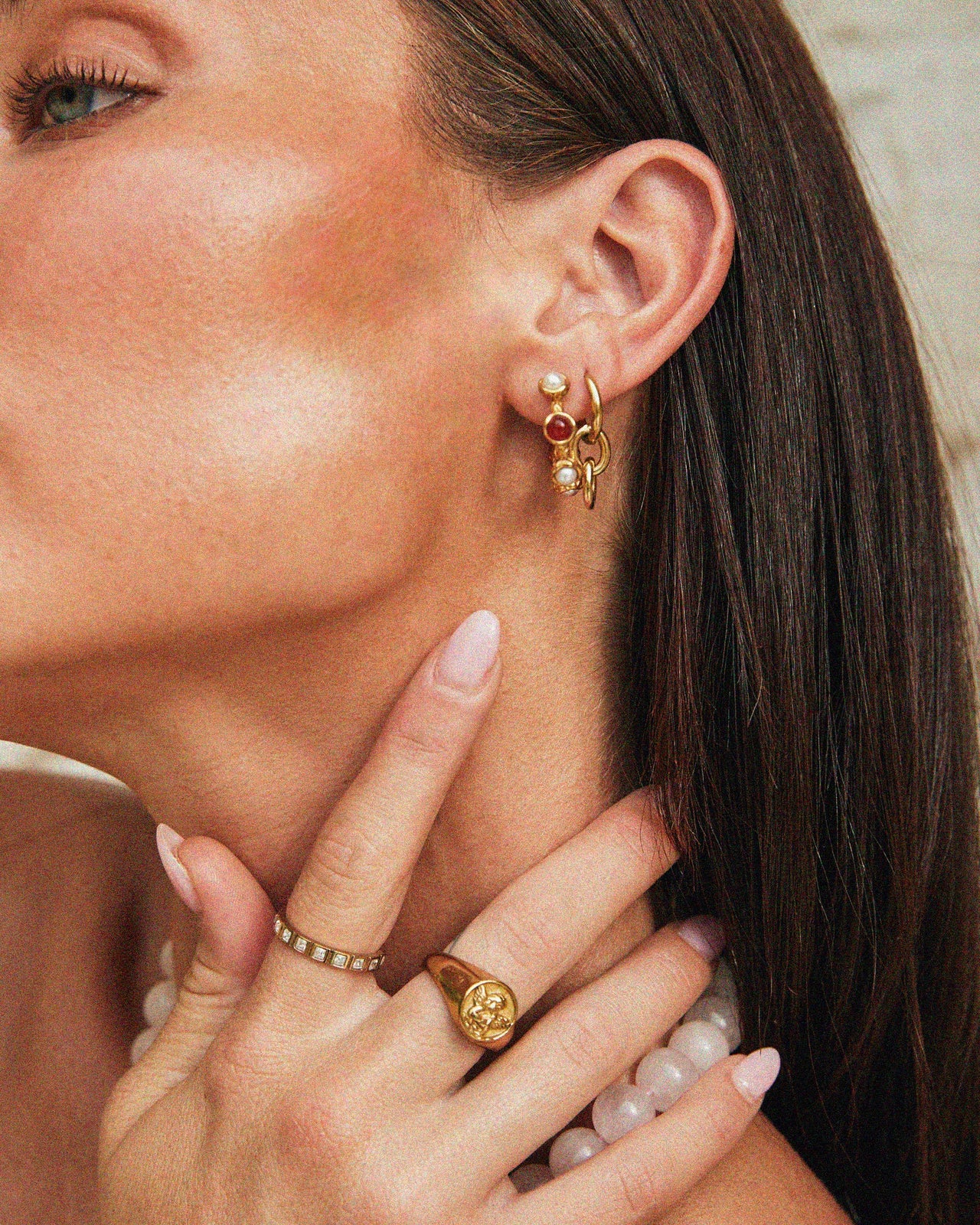 Close-up of a Tilly Smith wearing gold earrings and rings with a neutral background