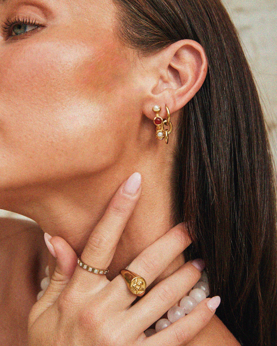 Close-up of a Tilly Smith wearing gold earrings and rings with a neutral background