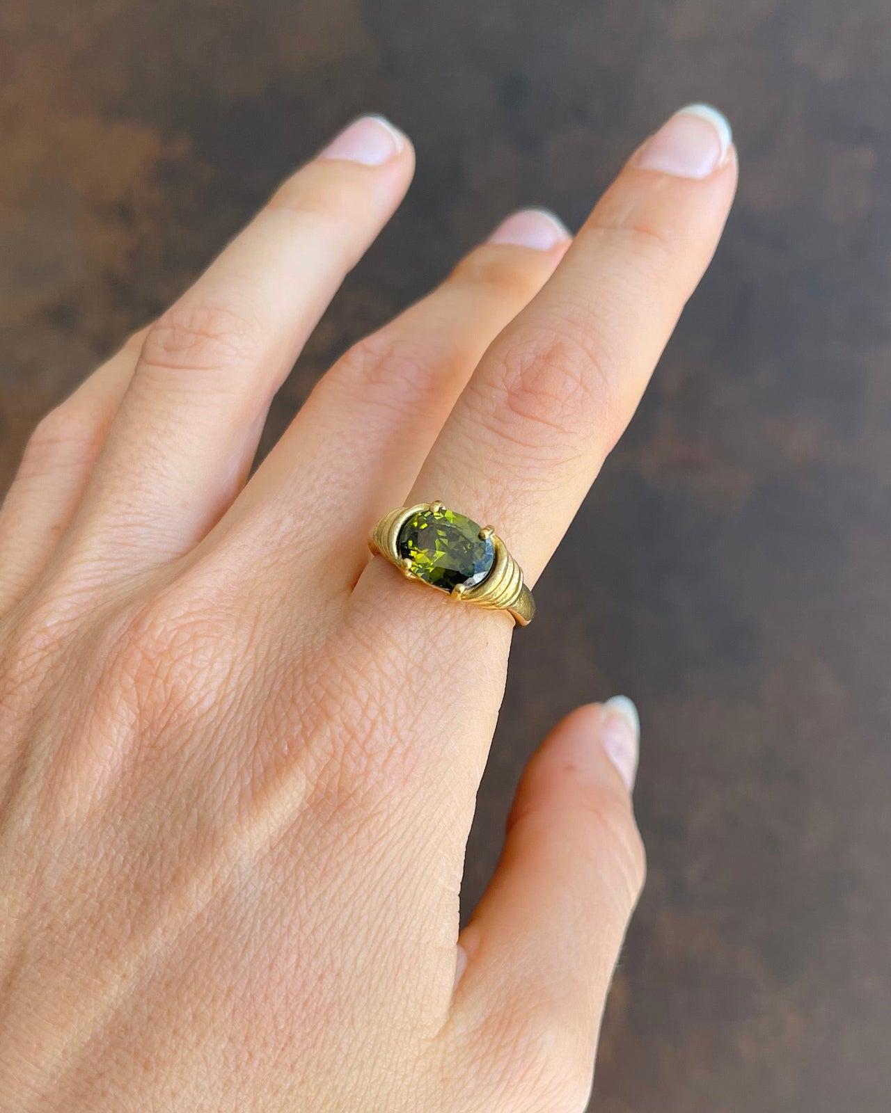 Hand wearing a gold ring with a green gemstone on a dark background
