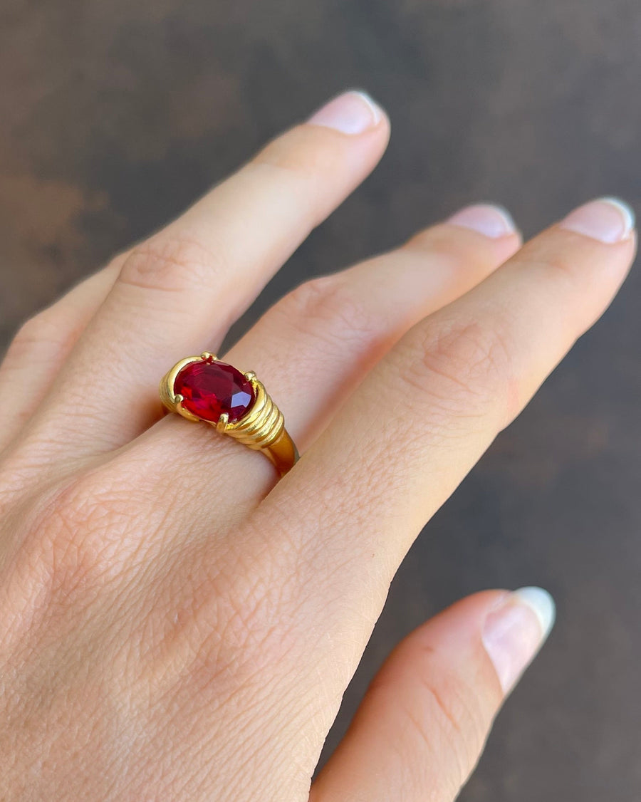 Gold ring with a red gemstone on a neutral background