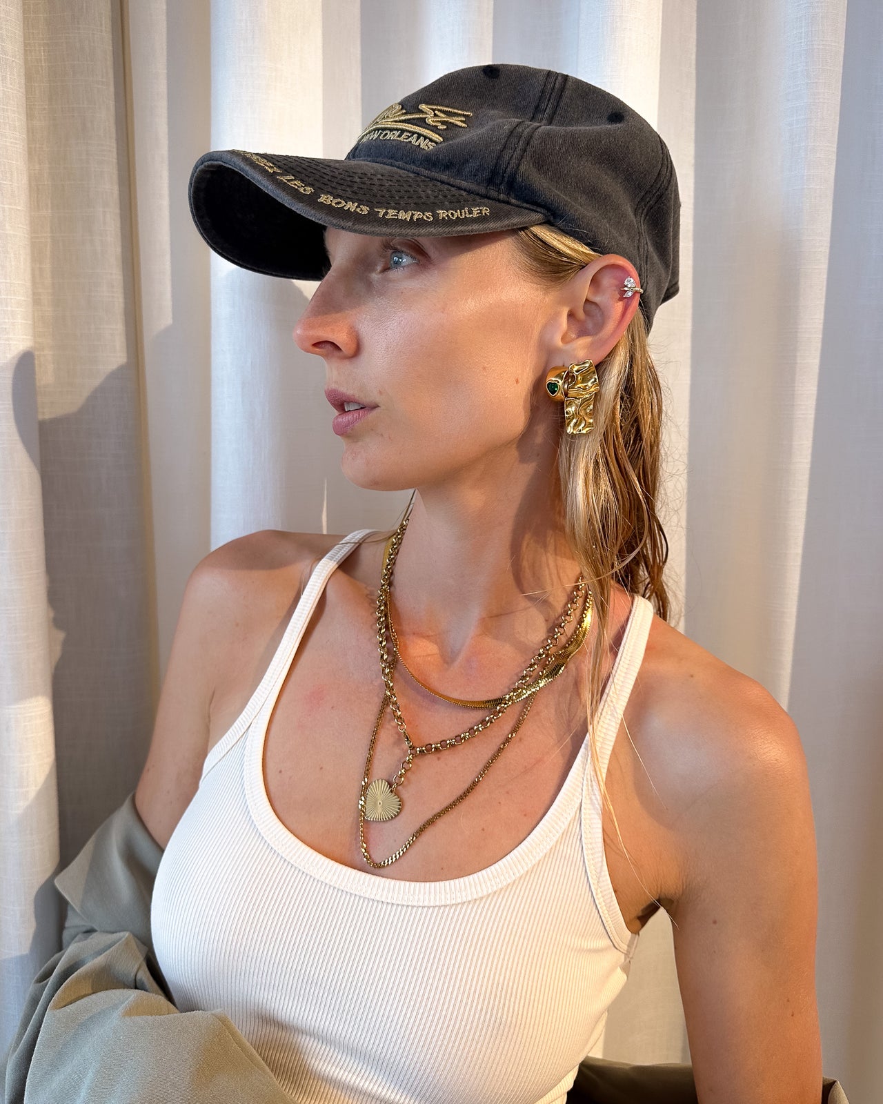 Woman wearing a black cap and white tank top with jewelry, sitting indoors.