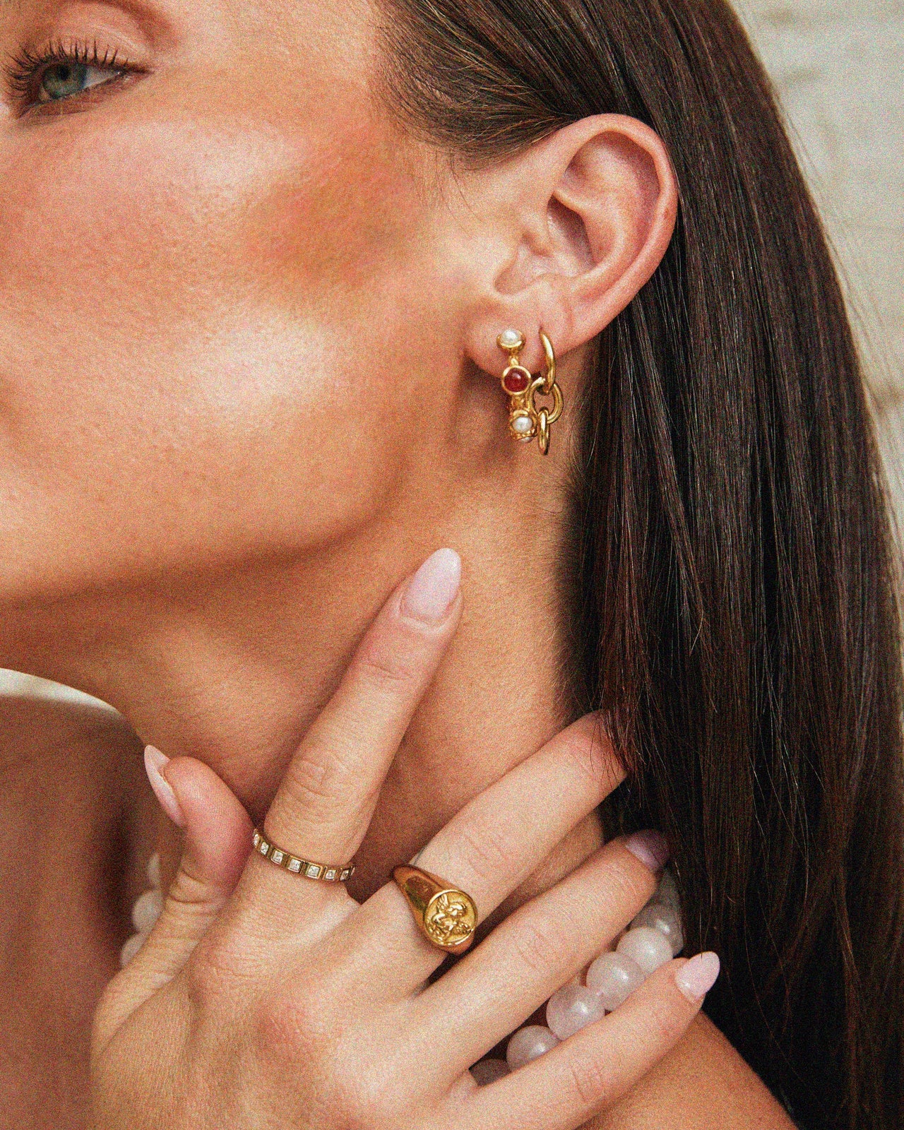 Close-up of a Tilly Smith wearing gold earrings and rings with a neutral background