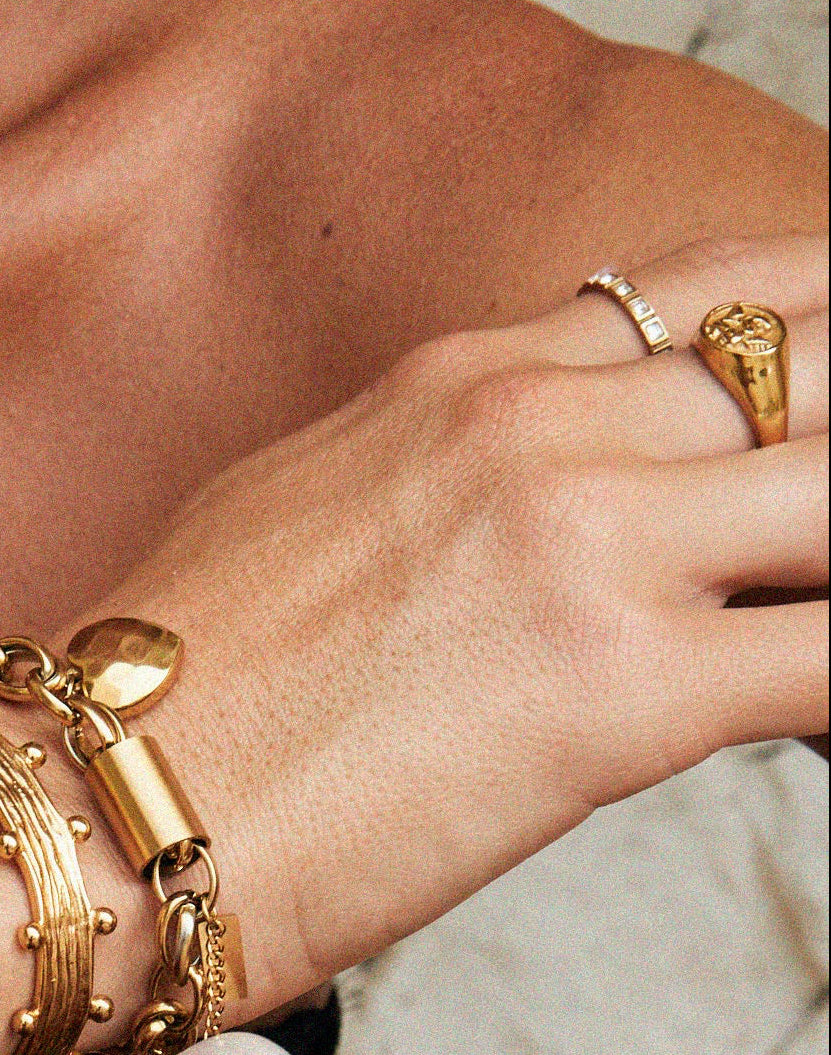 Close-up of a person wearing gold bracelets, a pearl necklace, and a large wooden bracelet.