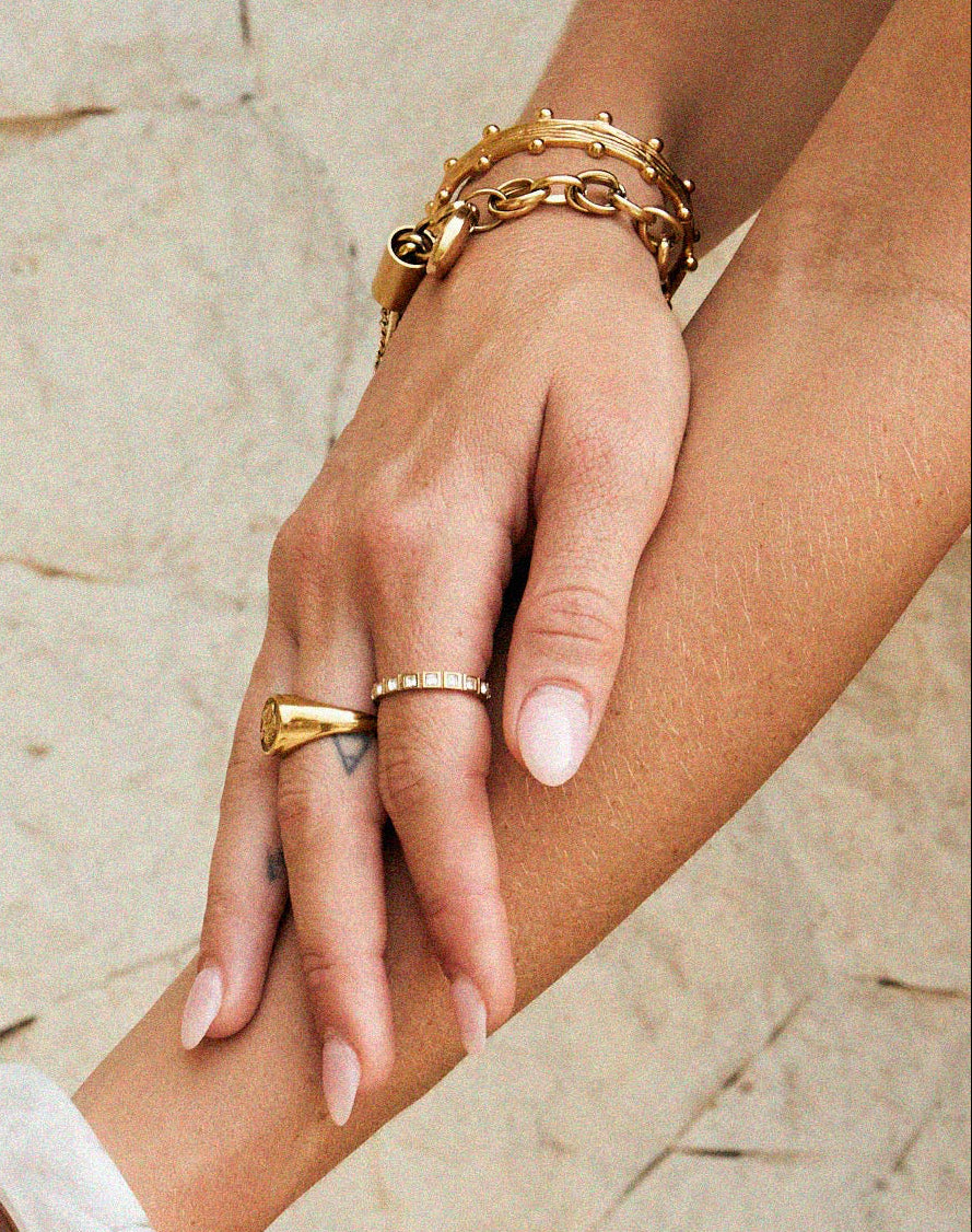 Close-up of a Tilly smith hand with multiple bracelets and rings on a stone surface