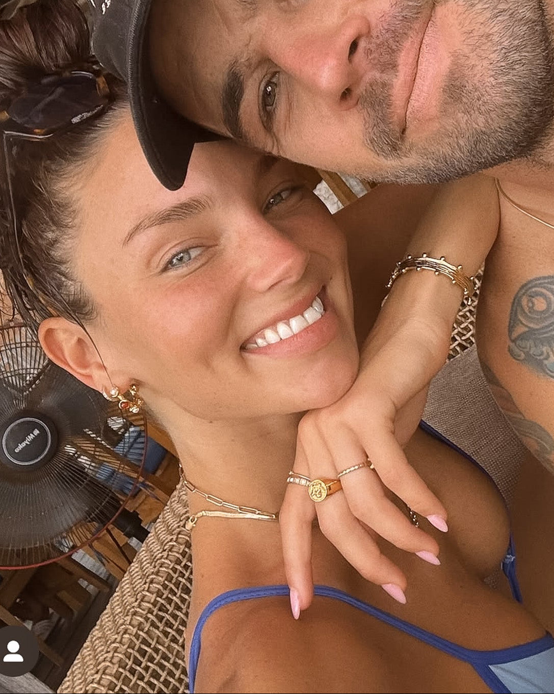 Man and woman posing closely together in a casual setting with wooden beams and hanging plants.
