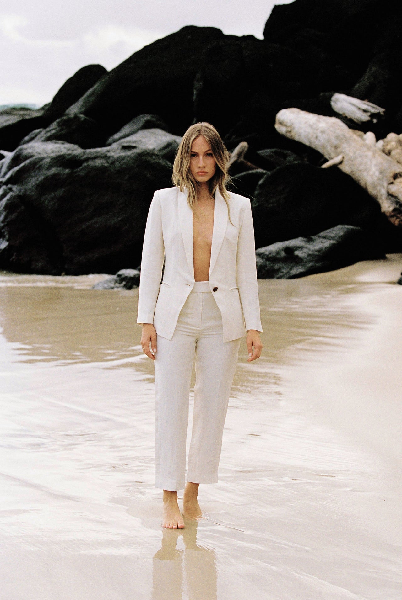 Model wearing white linen suit posing by the beach