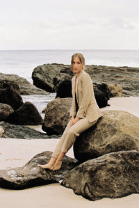 Thumbnail for Model wearing a taupe linen blazer and trouser posing on a rock by the beach