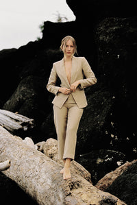Thumbnail for Model wearing a taupe linen blazer and trouser posing on a log by the beach