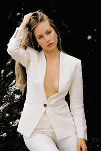 Thumbnail for Model wearing a white linen suit posing on a rock by the beach