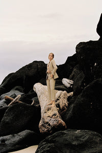Thumbnail for Model wearing a taupe linen blazer and trouser posing on a log by the beach