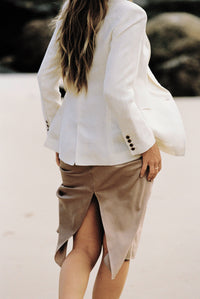 Thumbnail for Close-up of the back of a model wearing a white blazer and taupe silk slip skirt on the beach