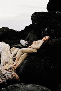 Thumbnail for Model wearing a taupe linen blazer and trouser posing on a rock by the beach