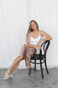 Thumbnail for Model wearing a white silk camisole and taupe silk slip skirt posing on a chair in a studio