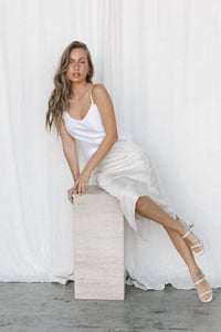 Thumbnail for Model wearing white silk camisole and cream silk skirt posing on a marble plinth in a studio