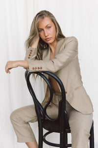 Thumbnail for Model wearing a taupe blazer and trouser sitting backwards on a chair in a studio